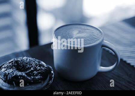Kaffee mit einem gezeichneten Herz und Milch auf einen hölzernen Tisch in einem Kaffee. Farbe des Jahres Konzept 2020. Schließen oben. Donut mit Streuung auf den Tisch neben Stockfoto