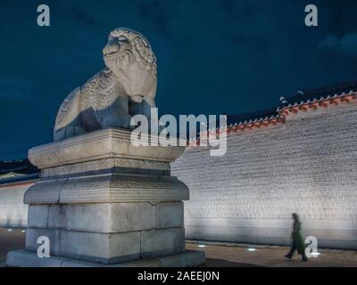 Person zu Fuß vorbei an Wand und riesige Statue, shishi Lion dog Guardian, außerhalb Gyeongbokgung Palast, night street, Seoul, Südkorea Stockfoto