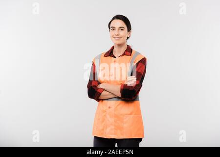 Glückliche junge Ingenieurin in Arbeitskleidung und orange Jacke überqueren, um die Arme Brust Stockfoto