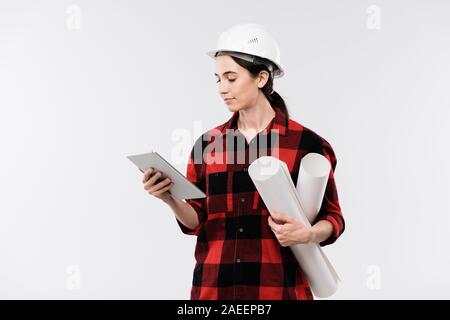 Junge schwere Ingenieurin in der Berufsbekleidung und Schutzhelm mit Touchpad Stockfoto