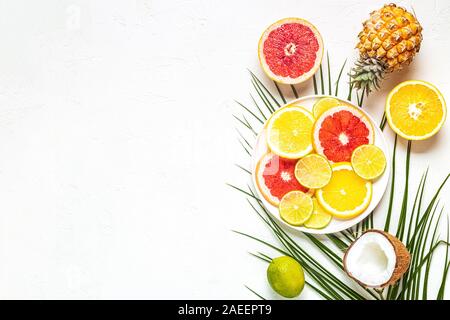 Tropische Früchte und Palmblättern auf einem weißen Hintergrund, Ansicht von oben. Stockfoto