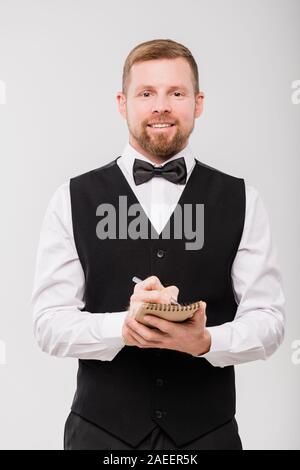 Glückliche junge Kellner in bowtie und schwarze Weste aufzuschreiben, damit der Client Stockfoto