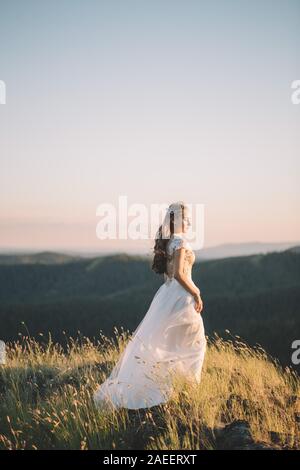 Brünette Frau in Weiß gewellt Kleid im Wind in den Bergen, Seitenansicht. Bildende Kunst, Hochzeit, Glück, Leben, Liebe, Leben Konzept Stockfoto