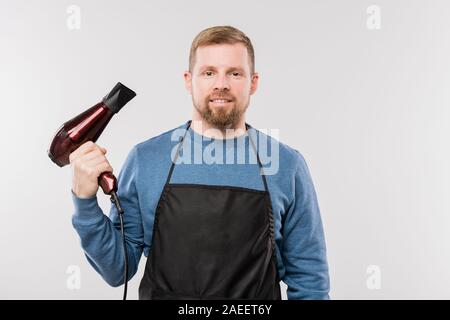 Junge Bartgeier Friseur in Schürze und blauen Pullover mit Haartrockner Stockfoto