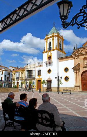 Ansicht der Socorro Pfarrkirche in der Plaza del Socorro mit Menschen sitzen auf einer Bank im Vordergrund, Ronda, Spanien. Stockfoto