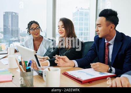 Fröhliche muti-ethnischen Business Team Diskussion Bericht über digitale Tablet beim täglichen Brainstorming Stockfoto