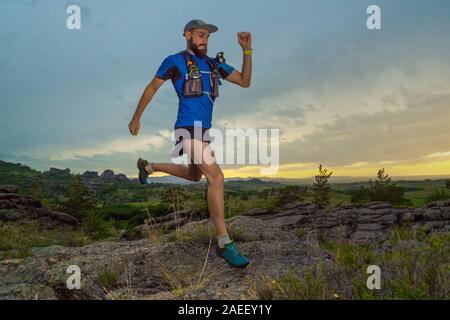 Eine männliche Läufer verläuft entlang einer Mountain Trail. Mann in einem blauen Pullover und in schwarzen Shorts. Das Training im Freien am Abend. Stockfoto