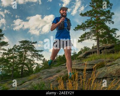 Eine männliche Läufer verläuft entlang einer Mountain Trail. Mann in einem blauen Pullover und in schwarzen Shorts. Das Training im Freien Stockfoto