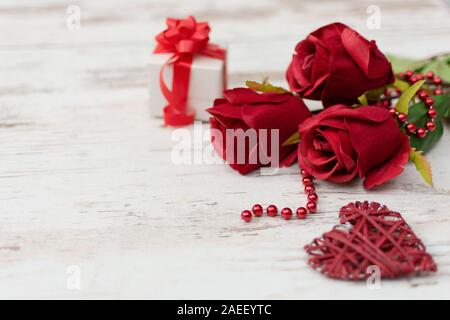 Rote Rosen, Geschenkbox und Holz dekoriert Hören auf weißem Holz- Hintergrund. Grußkarte. Kopieren Sie Platz. Stockfoto
