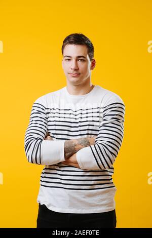 Junge groß schöner Mann in einem gestreiften Hemd mit Händen croosed über Gelb Stockfoto