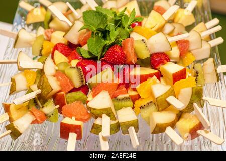 Stück Erdbeeren, Äpfel, Kaki, Birnen aufgereiht auf Holzstäbchen dekoriert Minze. Stockfoto
