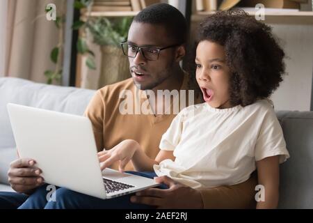 Schwarze Vater und Tochter überrascht mit Laptop zu Hause Stockfoto