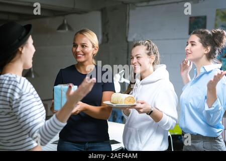Drei fröhliche junge Frauen gratulieren Ihrer Kollegin zu ihrem Geburtstag Stockfoto