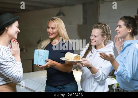 Gerne Kolleginnen gratulieren junge Frau und ihre Kuchen und Geschenke Stockfoto