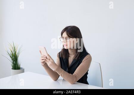 Junge brunette Geschäftsfrau in Smart Casual blättern in Smartphone im Büro Stockfoto
