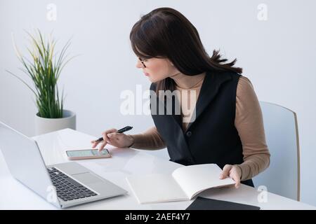 Junge erfolgreiche Geschäftsfrau mit offenen copybook Scrollen in Smartphone Stockfoto