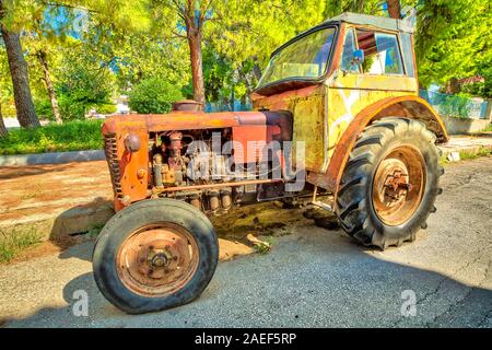 Seitenansicht einer alten gelben vintage Traktor mit abgebrochenen Rad in einer alten Straße aufgegeben. Stockfoto
