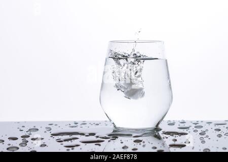 Würfel aus Eis in ein Glas Wasser mit Spritzern und Tropfen auf einen Spiegel schwarze Oberfläche Stockfoto