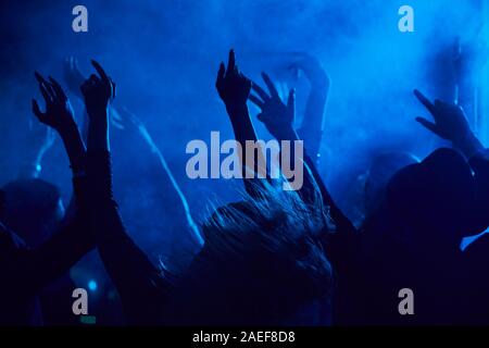 Silhouetten von Jugendlichen springen und heben die Hände beim Genießen der Musik Konzert in verrauchten Nachtclub durch blaues Licht leuchtet, kopieren Raum Stockfoto