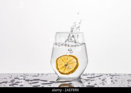 Ein Glas Wasser mit einer Zitronenscheibe auf einem Spiegel Hintergrund auf schwarzem Hintergrund Stockfoto