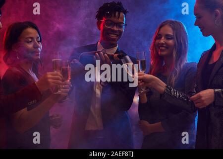 Gruppe von fröhlichen jungen Menschen gießen Champagner in verrauchten Nachtclub und genießen Sie Partei Stockfoto