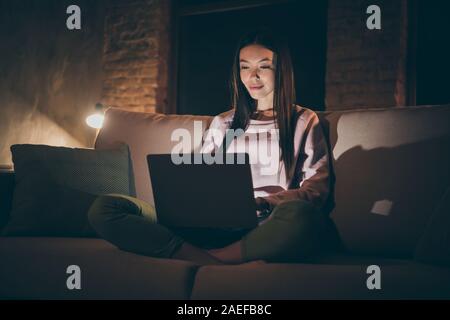 Foto von homey chinesische Frau notebook Knie texting zuständigen Kollegen Nachtarbeiter Sit Comfort couch casual Outfit dunklen Wohnzimmer Stockfoto