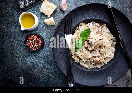 Risotto mit Pilzen in einer schwarzen Platte über dunklen Hintergrund, Ansicht von oben Stockfoto