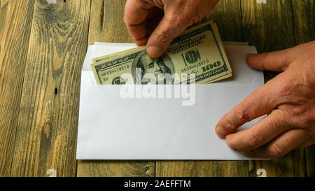 Menschliche Hände zwei hundert Dollarscheine in bar in weißes Papier Umschlag, der auf braune Holztisch liegt. Konzept der Geld sparen oder Korruption Stockfoto