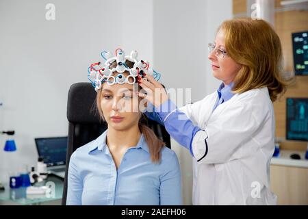 Weibliche Wissenschaftler, der Gehirnwellen setzt scannen Helm auf einem weiblichen Patienten. Moderne Audiosystem und Technologie Stockfoto