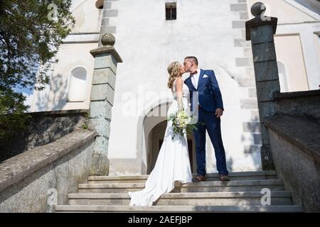 Der Kuss. Braut und Bräutigam Küsse zärtlich auf einer Treppe vor einem kleinen lokalen Kirche. Stockfoto