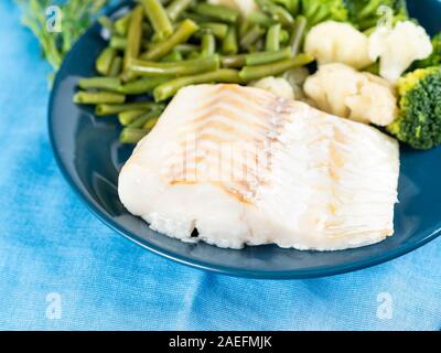 Filet von der gekochten Seefisch Kabeljau mit Brokkoli, grüne Bohnen und Blumenkohl auf einem blauen Platte, Seitenansicht, schließen. Gesunde Diät Teller für richtige Ernährung Stockfoto