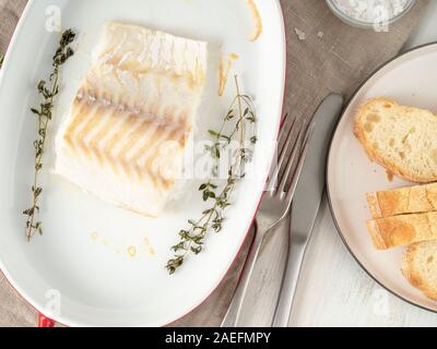 Kabeljau Fisch Filet, frisch im Backofen gekocht mit Thymian in einer porzellanschale zum Backen, Brot auf den Teller, Ansicht von oben Stockfoto