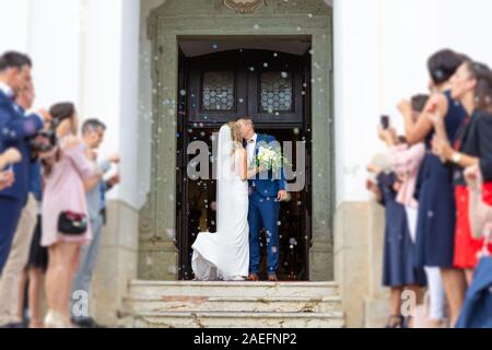 Brautpaar küssen beim Verlassen der Kirche nach der Trauung, Familie und Freunde feiern ihre Liebe mit der Dusche der Seifenblasen, Custom Stockfoto