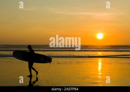 Silhouette einer Surfer mit seinem Surfbrett am Strand von Kuta auf einen goldenen Sonnenuntergang Stockfoto