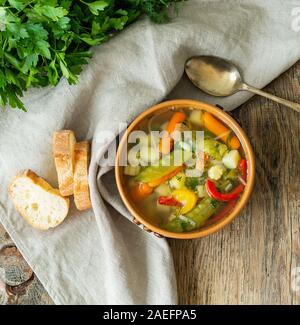 Helle Frühling pflanzliche Ernährung vegetarische Suppe mit Kartoffeln, Paprika, Karotten, Erbsen, Petersilie. Ansicht von oben, Braun rustikale Holz Hintergrund, Bettwäsche napk Stockfoto