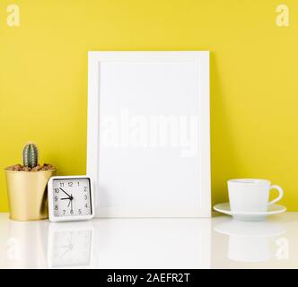 Leeren weißen Rahmen, Uhr, saftig, Becher mit Tee oder Kaffee gegen die gelbe Wand. Mockup mit kopieren. Stockfoto