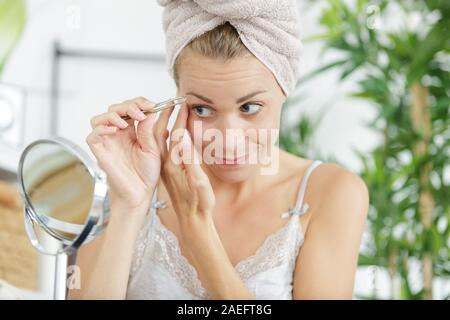 Frau Zupfen der Augenbrauen durch das Fenster Stockfoto