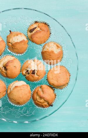 Leckere hausgemachte Vanille Muffins mit Schokolade auf die Glasplatte auf Türkisfarbenem Hintergrund. Süße Nachspeise für Feier, Party oder einen Snack. Cupcakes. Stockfoto