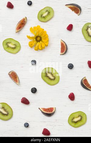 Draufsicht auf Schnitt Sommer Obst (Feigen, Kiwis, Himbeeren, Heidelbeeren) und Blüten auf weiß Holz- Hintergrund. Gesunde Ernährung Konzept Stockfoto