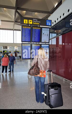 Frau mit einem Koffer ständigen Lesen der Flight Information Display im Terminal 3 am Flughafen Malaga, Malaga, Spanien. Stockfoto