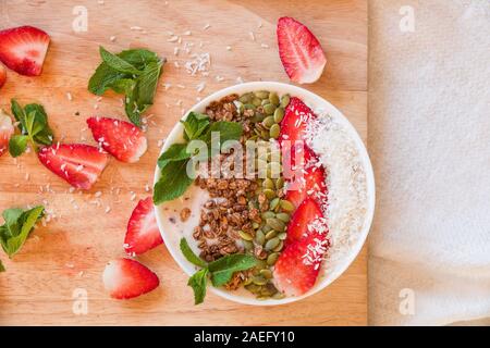 Frühstück Berry Smoothie Schüssel gekrönt mit Erdbeere, Kürbiskerne, Kokos, Müsli und frischer Minze. Strawberry Banana Smoothie Schüssel. Gesunde Breakfas Stockfoto