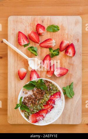 Frühstück Berry Smoothie Schüssel gekrönt mit Erdbeere, Kürbiskerne, Kokos, Müsli und frischer Minze. Strawberry Banana Smoothie Schüssel. Gesunde Breakfas Stockfoto