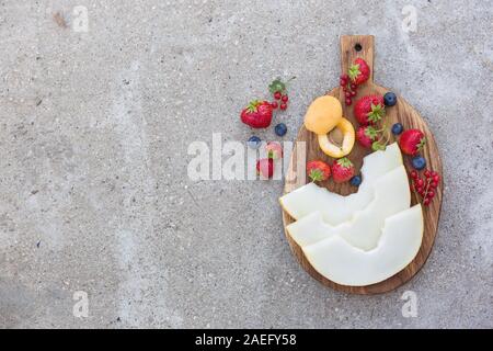 Draufsicht auf Holzbrett mit frischem Obst und Beeren: Melone, Erdbeeren, Blaubeeren, Apricot und Rot aktuelle auf konkreten Hintergrund. Gesundheit Stockfoto