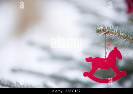 Schöne rote Dekoration - Red Horse - hängend am Weihnachtsbaum Zweig im Freien an einem sonnigen Tag. Winter. Urlaub Konzept Stockfoto