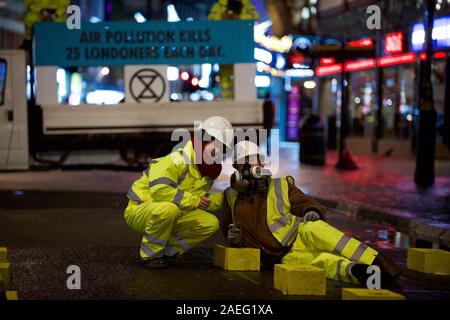 London, Großbritannien. 09 Dez, 2019. Aussterben Rebellion' Luft, die wir trauern' protestieren Demonstrant eine pre-dawn Aktion in Central London illegalen die Luftqualität in der Hauptstadt zu protestieren. Die Autobahn Wartung Arbeiter gekleidet, sie blockiert Cranbourne St und sich für konkrete Bausteine auch auf der Straße Credit geklebt geklebt: Gareth Morris/Alamy leben Nachrichten Stockfoto