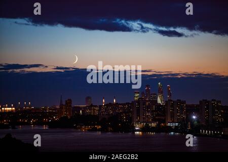 Nachts oder abends Stadtbild mit Wolkenkratzern und Stadt Silhouette am Fluss in tiefem Blau und Gelb Himmel mit Wolken und Crescent. Stockfoto