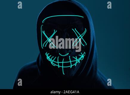 Porträt eines anonymen Mann in einem schwarzen Kapuze sein Gesicht versteckt sich hinter einem furchtsamen neon Mask. Studio gedreht. Stockfoto