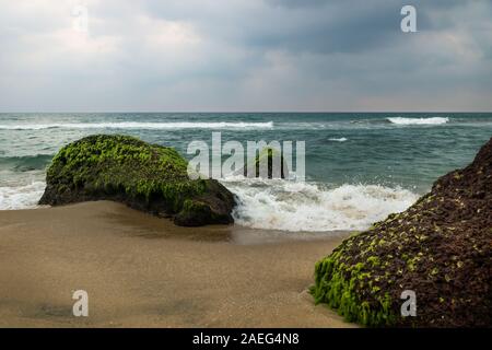 Spritzer Welle entlang Coastside auf grünem Moos vulkanischen Steinen von Varkala mit dunklen cloudscape, Indien Stockfoto