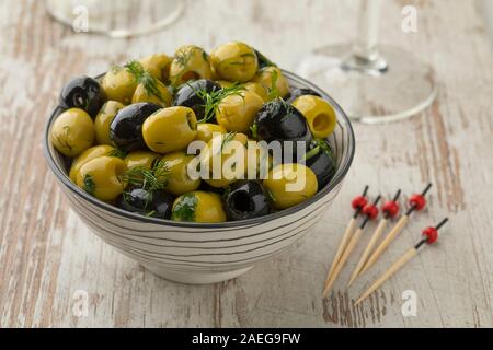 Schüssel mit grünen und schwarzen Oliven, gewürzt mit frischen Kräutern Nahaufnahme Stockfoto