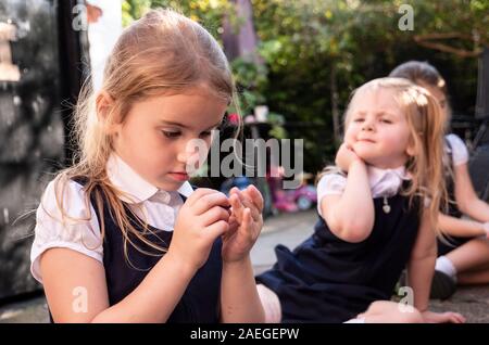 Ein kleines Mädchen trägt Schuluniform tief in Gedanken mit Ihre Schwestern im Hintergrund Stockfoto